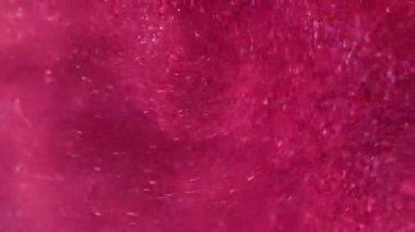 Parıltılı bir dönüş. Parlak sıvı. Odaklanmamış pembe renkli parlak toz parçacıkları su mürekkebi emülsiyon girdaplı soyut sanat arka planında titreşir.