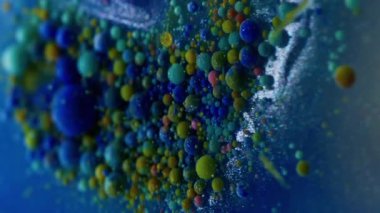 Dikey video. Yağ sıvısı. Su damlasını boya. Mavi suda yüzen odaksız renkli kabarcıklar. Patlayan jel dokusu serumu soyut sanat arkaplanı.