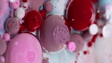 Dikey video. Baloncuk döküldü. Mürekkep akışı. Yağ rengi damlaları suda çözünüyor. Kırmızı pembe beyaz akrilik pigmeler köpük soyut sanat arka planı.