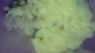 Mürekkep bulutu. Renk sıçraması. Pastel sarı boya damlası mor suda çözünür. Sıvı sanat akışları soyut odaklanmış arka planda dumanlı çekim yapar.