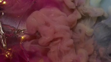Dikey video. Parıltılı akış. Boya patladı. Çok renkli duman kıvrımları garip bir şekilde ışıl ışıl sanat sıvısı arka planlarını karıştırıyor. Peçe dumanı pembe su ampulü kırıldı..