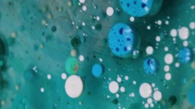 Dikey video. Boya jeli. Yağ kabarcıkları. Turkuaz pigment topları saydam bulanık sanat sıvısı mermer mavi su soyut arka plan derinliğinde yüzüyor.