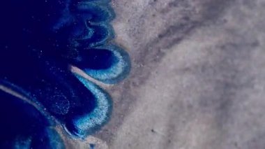 Boya dökülmüş. Parıltı karışımı. Parlak mavi lekeli sıvı gümüş gri parıldayan parçacıkların yüzeyine yayılmış. Kontrast rengi soyut odaklanmış arkaplan.