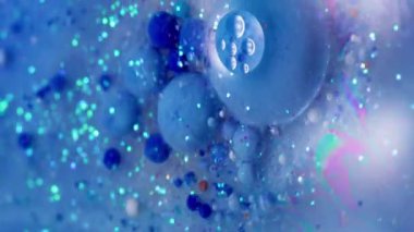 Dikey video. Işıldayan akış. Akrilik baloncuk. Parıldayan parçacıklar renkli boya karışımı. Mavi gökkuşağı suyu soyut arkaplanı döker.