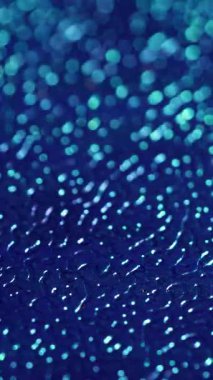 Dikey video. Bokeh dokusu. Yapay deri. Mavi dalgalı plastik yüzey rahatlaması ve değişen ışık. Dekoratif bulanık parlak parlamalı kabartmalı arkaplan.