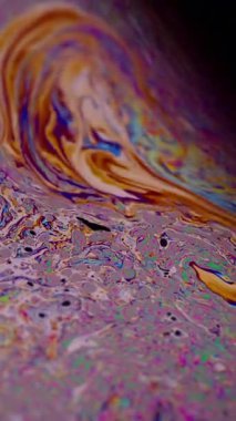 Dikey video. Yanardöner sıvı. Sıvı damlalar akar. Odaklanamayan mor renkli, yeşil yağlı boya eğrisi koyu siyah, aydınlık, soyut sanat arka planında akrilik kaygan..