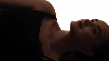 Dikey video. Güzellik silueti. Yüz hatları. Tatmin olmuş, pohpohlanmış, beyaz tenli, gülümseyen bir kadının koyu renk kontrastı.