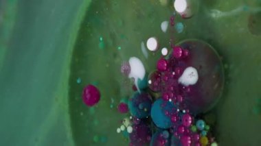 Dikey video. Yağ sıvısı. Mürekkep patladı. Parıldayan sızıntı, şeffaf dairesel pigment renk baloncukları. Yeşil mor sanat soyut arkaplan.