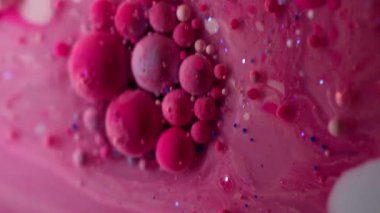 Dikey video. Boya jeli. Yağ kabarcıkları. Pembe pigment topları saydam bulanık sanat sıvısı mermer içinde yüzüyor. Suyun soyut arkaplanı parıldıyor. .
