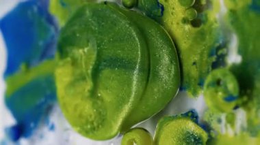 Dikey video. Işıldayan akış. Parlak boya damlası. Pudra suyuna dökülen renkli akrilik jel. Yeşil mavi sıvı karışımı soyut arkaplan.