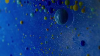 Dikey video. Mavi akış. Kabarcık emülsiyonu. Parlayan suda yüzen çok renkli akrilik küreler. Soyut arkaplanda mürekkep damlası karışımı.