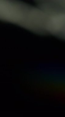 Dikey video. Büyüleyici soyut doku. Bulanık gökkuşağı gölgeleri. Odaklanamayan sızıntı, çok renkli yeşil ışınlar, siyah sanat ışığı arka planında yanıp sönen ışın mercekleri..