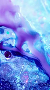 Dikey video. Leylak akıntısı. Buzda boya. Sıvı mor suluboya donmuş mavi yüzeyde akar. Soğuk bulanık mor boya karışımı dalgalı bir şekilde dökülüyor..