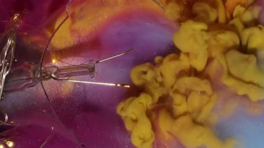 Dikey video. Boya fırçası. Parlak duman. Pembe parıldayan sanat sıvısını karıştıran turuncu duman spreyi. Açık renk çelenk kırık ampul soyut su arkaplanı.