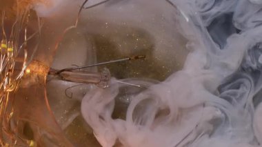 Dikey video. Pırıltılı sis. Sanat buharı. Işıldayan hipnotik beyaz akarsu dalgalı mürekkep suda karışıyor. Parıldayan parçacıklar soyut arkaplan bulutları..