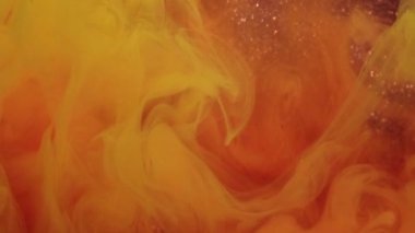 Sis sıvısı. Sarı akış. Parlak turuncu boya bulutu, altın rengi parlak ve soyut arka planda dönüşümlü olarak dönüyor. Suda şeffaf dumanlı bulanık peçe boyası.