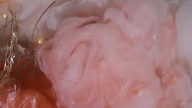 Dikey video. Duman patladı. Boya karışımı. Parlak turuncu mat beyaz sanat sıvısı akıntıları. Kırık ampulün üzerinde çakışan dumanlı mürekkep spreyi..