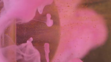 Dikey video. Küre parçacıkları. Mürekkep sıçraması. Soyut sanat arka planına yayılan pembe altın rengi boya damlası..