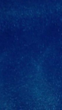 Dikey video. Parıltı soyut bir arkaplan. Bulanık pırıltılı girdaplar. Beyaz renkli toz parlak parçacıklar parlıyor mavi ışıkta dönen mürekkep akışı yıldız illüzyonu..