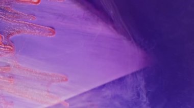 Dikey video. Boya damlası. Işıldayan damlalar. Mor üçgen üzerinde kayan turuncu simli damlalar renkli dumanlı su arkaplanı bulanıklaştırır.