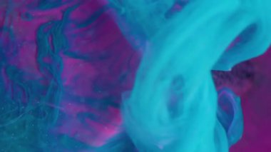 Dikey video. Mistik sıvı. Neon boya. Parlak mavi boya akışı pembe mor cam küp yüzeyine yayıldı. Yağlı su pigment karışımı soyut arkaplan bulanıklığı.