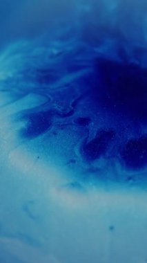 Dikey video. Yağ akışı. Bulanık mürekkep dokusu. Parıldayan mavi beyaz parçacıklar boya damlası dalgası soyut sanat arka planına düşüyor.