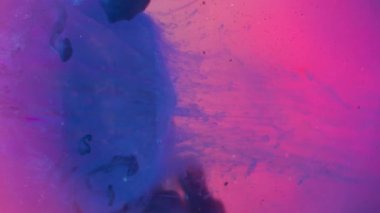 Dikey video. Odaklanamayan damlama. Elmas değerli taş. Kesimli yuvarlak kristalin pembe mor sıvısı düşüyor. Çember neon bulanık mor mavi soyut su arkaplanındaki boya karışımı.