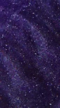 Dikey video. Görüntü pırıl pırıl parlıyor. Parıldayan parçacıklar. Parlak mor beyaz renkler parlak parlak parçalar boya mürekkebi kıvrımları koyu soyut arkaplanda hareket ediyor.