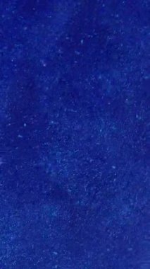 Dikey video. Bulanık tozu. Toz dokusu. Işıl ışıl parlayan beyaz parçacıklar soyut koyu mavi arka planda dönen parlak sisli boya mürekkebi..