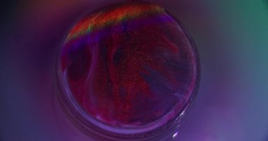 Gökkuşağı alevi. Hafif emülsiyon. Odaklanmamış kırmızı mavi renkli yuvarlak mürekkep simli gökkuşağı desenli damlacıklar soyut neon mor arka planda sızıyor.