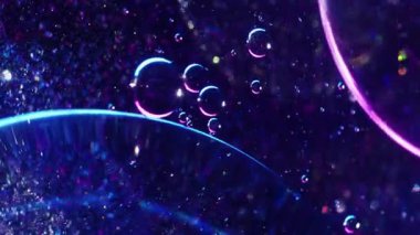 Floresan kabarcıkları. Parıldayan özü. Odaklanmamış mavi neon renkli yağ damlası koyu soyut arkaplanda daireler çiziyor..