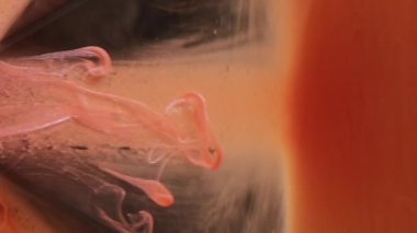 Dikey video. Haze düşüşü. Duman akışı. Suda yüzen parlak turuncu mürekkep peçesi. Siyah parlayan piramit üzerinde kayan parlak boya soyut arkaplan bulanıklığı.