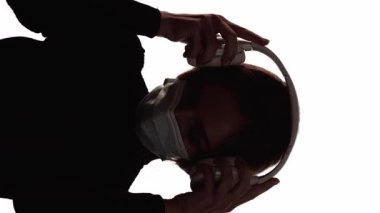 Dikey video. Karantina müziği. Kulağa hoş geliyor. Yüz maskeli bir kadının silueti, kulaklıkla, bokeh ışıklarıyla, beyaz ışıklarla, rahatlatıcı sesleri dinlemekten zevk alıyor..