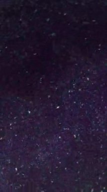 Dikey video. Görüntü pırıl pırıl. Barut parçacıkları. Parlak parlak noktalar parıldayan toz, soyut mor arka planda kıvrılıp duruyor..