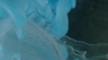 Dikey video. Sis mürekkebi. Küre şeklinde. Odaklanmamış mavi renk ıslak doku su sıvı akış boyası soyut sanatı koyu siyah arkaplan üzerine damlıyor.