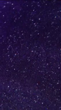 Dikey video. Bulanık kıvılcımlar. Yanıp sönen parçacıklar. Parlak beyaz renkler parıldıyor parlak parçalar fırıl fırıl dönüyor boya mürekkebi koyu mor soyut arka planda hareket ediyor.