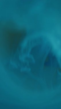 Dikey video. Bulanık renk sıvısı. Mürekkep damlası. Mavi, beyaz, pırıl pırıl parlıyor. Pürüzsüz, sisli çemberler, soyut modern arkaplanı aydınlatıyor..