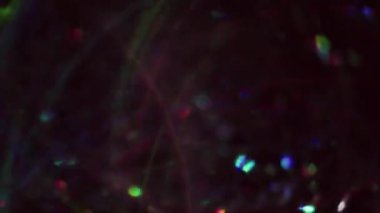 Bokeh ışığı. Odaklanmamış çelenk. Lens parlamaları ışık parçalarını kıvılcımlar. Bulanık siyah soyut arka planda yüzen çok renkli gölgeler..