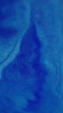 Dikey video. Parlak kıvılcımlar. Görünmez yağ akışı. Yanıp sönen mavi renk sıvısı parlayan sıvı boya mürekkebi parlak toz soyut bokeh ışık arka planında hareket ediyor.