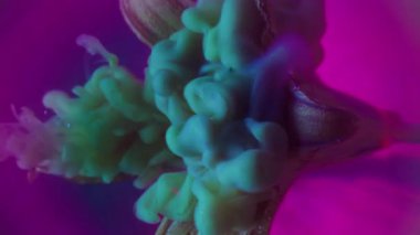 Dikey video. Mürekkep buharı. Çiçek dumanı. Taze nilüfer yapraklarının üzerine sanat sıvısı dökülmüş. Neon mor parıltı çemberinin arka planında bulanık çok renkli toz karışımı.
