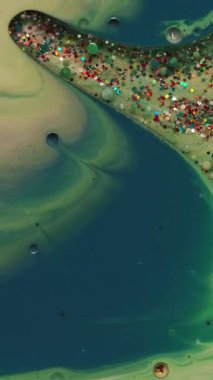 Dikey video. Mürekkep akışı. Sanat sıvısı. Yeşil sarı sıvı sızıntı, yağ lekesi, parıltı pudrası. Renk parçacıklarını soyut bulanık arkaplanla karıştır.