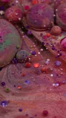 Dikey video. Mermer baloncuklar. Boya akışı. Fantezi gibi yuvarlak jel topları sanat yağı sıvısında fokurduyor. Pembe turuncu parçacıklar girdap şeklinde soyut arkaplan dökerler.