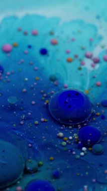 Dikey video. Baloncuk döküldü. Mürekkep akışı. Yağ renkli damlalar mavi sıvıda eriyor. Su soyut sanat arka planında yüzen akrilik pigmentler.