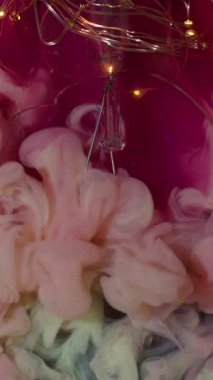 Dikey video. Yaratıcı duman. Boya dumanı. Pembe köpüklü suda peçe mürekkebi dalgalanması. Kırık parlak ampul dekoratif soyut arkaplan.