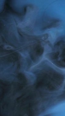 Dikey video. Dumanlı akış. Sis dokusu. Odaklanamayan koyu mavi duman bulutu soyut sanat arka planına boya mürekkebi sıvısı sıçratıyor..