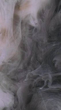 Dikey video. Bulut dumanı. Boya mürekkebi. Odaklanmamış gri renkli duman bulutu, soyut altın desenli arka plan üzerine sis dokusu sıçratıyor.