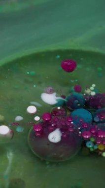 Dikey video. Yağ sıvısı. Mürekkep patladı. Parıldayan sızıntı, şeffaf dairesel pigment renk baloncukları. Yeşil mor sanat soyut arkaplan.