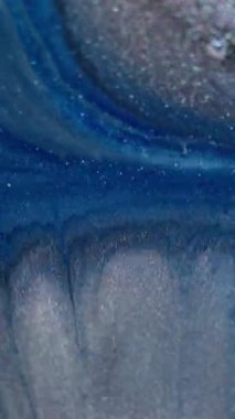 Dikey video. Parlak karışım. Mürekkep arkaplanı. Mavi gri gri toz akıntısı siyah yüzeye yayılıyor. Soyut simli boya parçacıkları bulanıklığı.