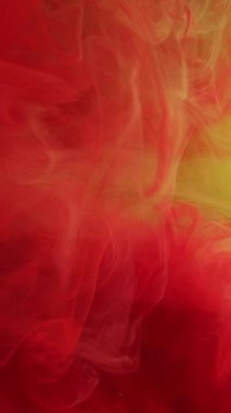 Dikey video. Sis sıvısı. Renk bulanıklığı. Kırmızı dumanlı boya, sarı suda pürüzsüz kıvrımlar oluşturur. Parlak suluboya damla pigmentleri soyut arkaplan karıştırılıyor.