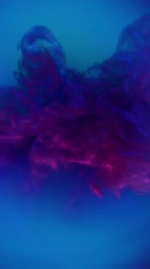 Dikey video. Boya patlaması. Parlayan toz. Mor menekşe rengi neon gazı mavi sıvıda patlamış. Gizemli su soyut arkaplan parıltısı.